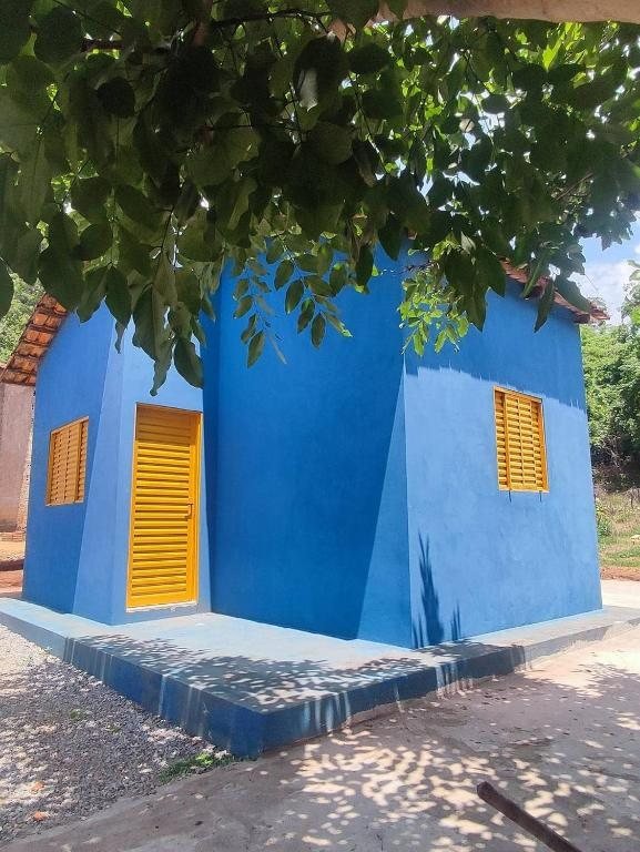 Fachada do Chalé Azul: paredes azuis, porta e janelas de veneziana amarela, embaixo de uma árvore